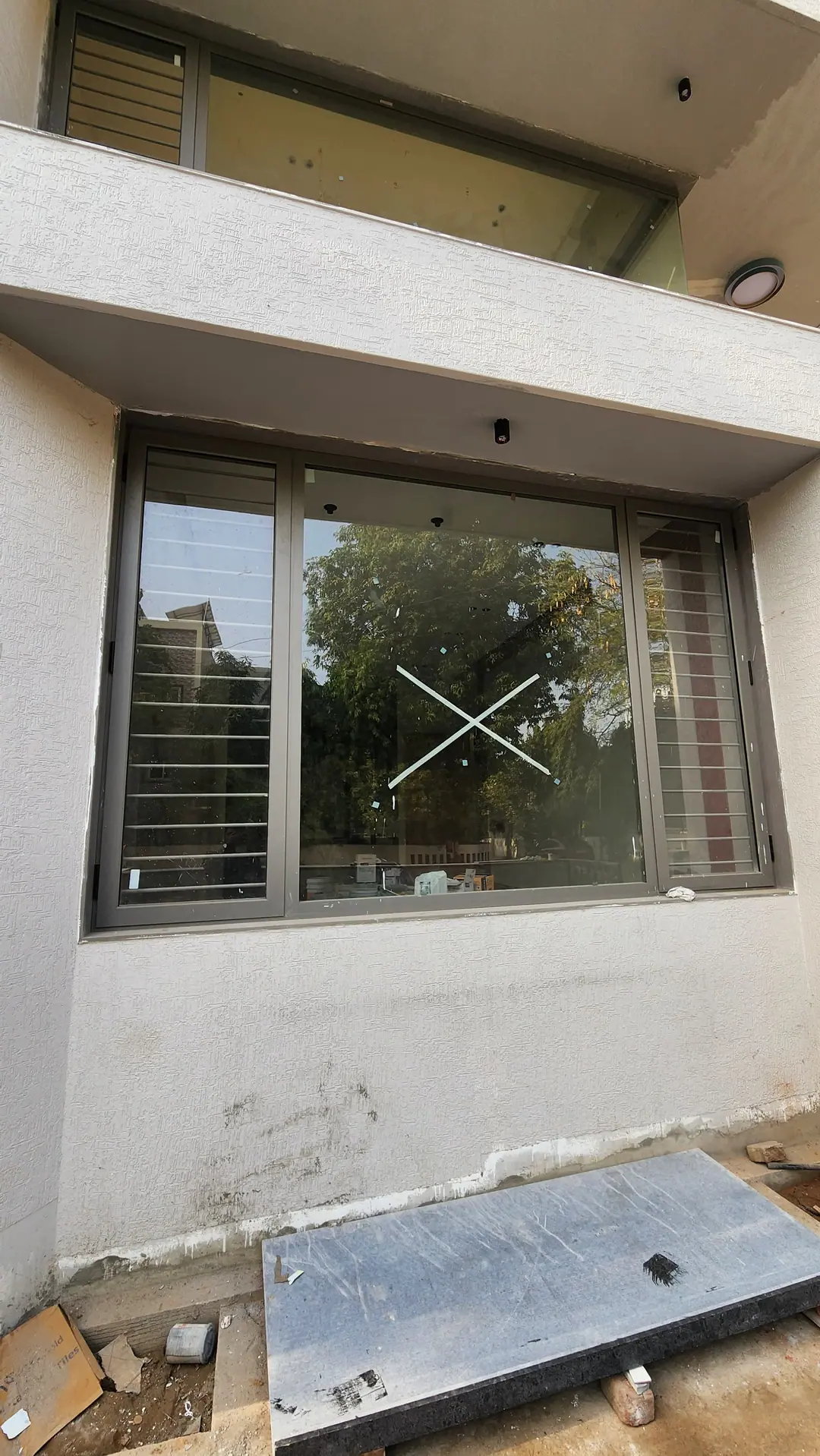 Grey aluminium sliding window with an insect mesh panel, fitted into the wall of a house under construction