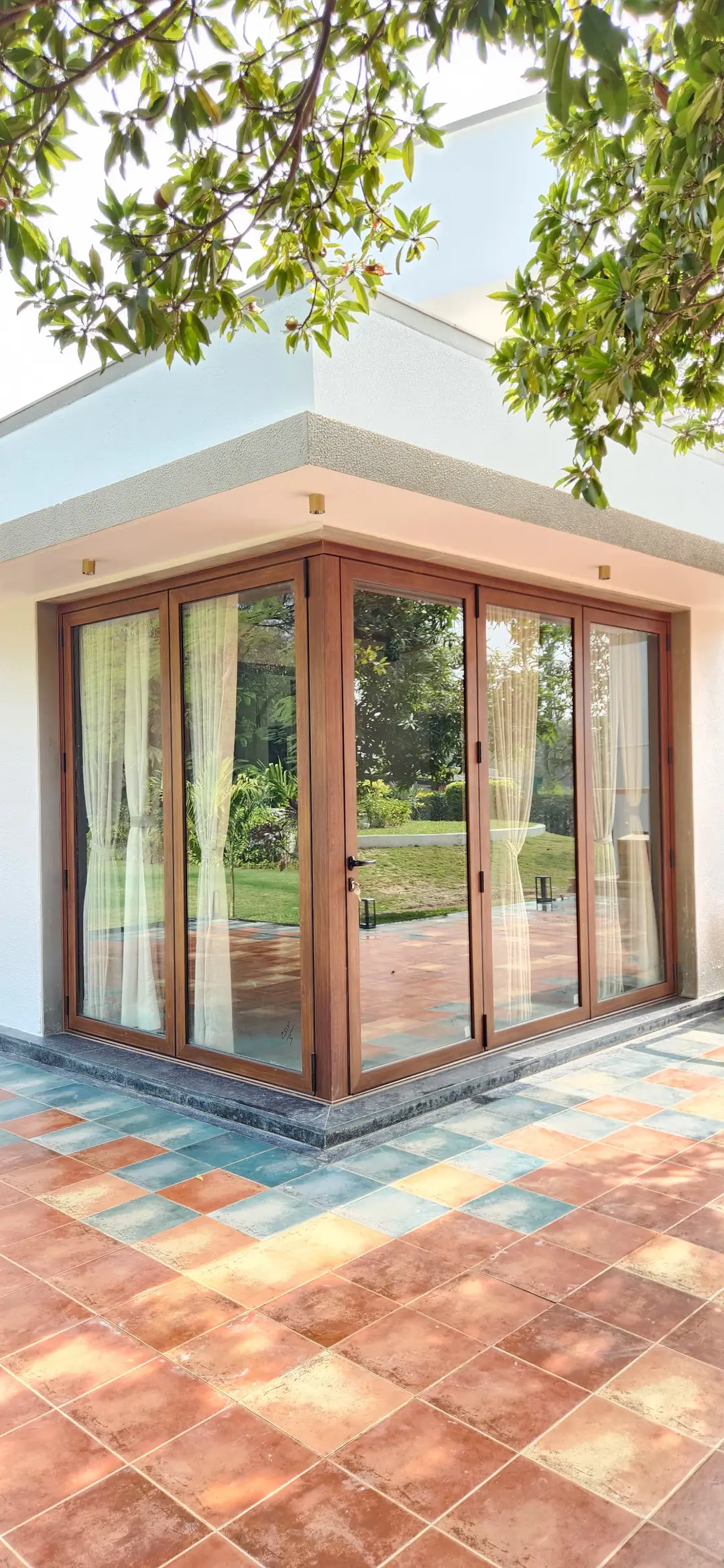 Wood-finish aluminium glazed doors wrapping the corner of a house, opening onto a terracotta-tiled patio and garden